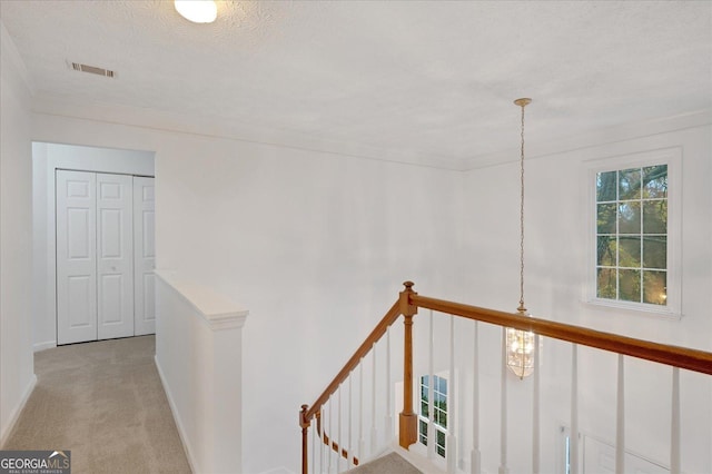 hallway featuring light carpet, ornamental molding, and a textured ceiling