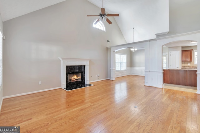 unfurnished living room with ceiling fan, a tiled fireplace, high vaulted ceiling, and light hardwood / wood-style flooring