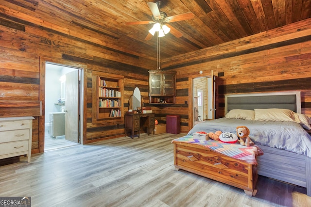 bedroom featuring wooden walls, ceiling fan, light hardwood / wood-style floors, and connected bathroom