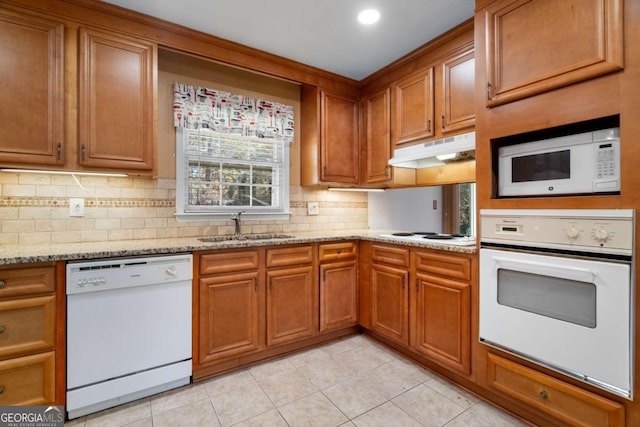 kitchen featuring tasteful backsplash, light stone counters, white appliances, sink, and light tile patterned floors