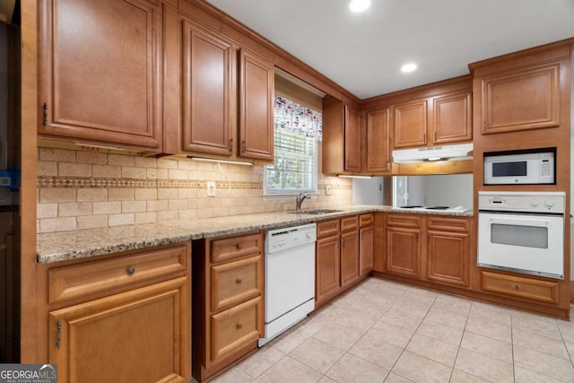 kitchen featuring light stone countertops, tasteful backsplash, white appliances, sink, and light tile patterned flooring