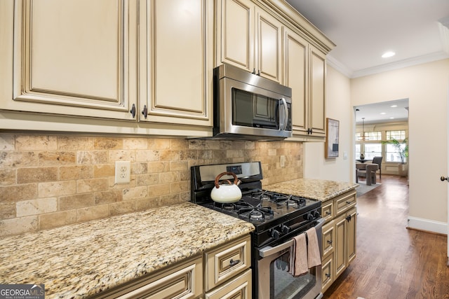 kitchen featuring backsplash, stainless steel appliances, light stone counters, cream cabinets, and ornamental molding