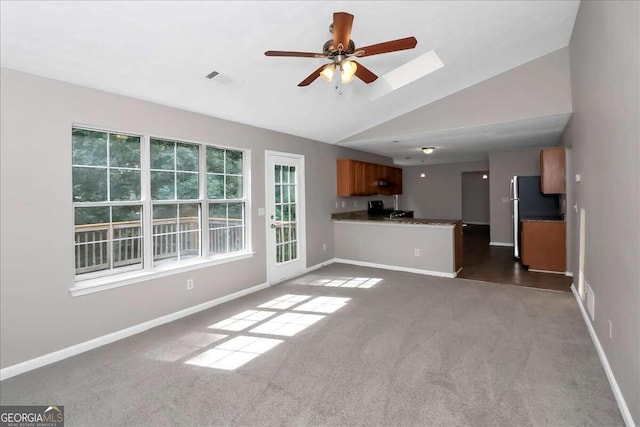 unfurnished living room with vaulted ceiling with skylight, ceiling fan, and dark colored carpet