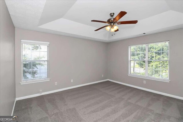 carpeted empty room with a raised ceiling and ceiling fan