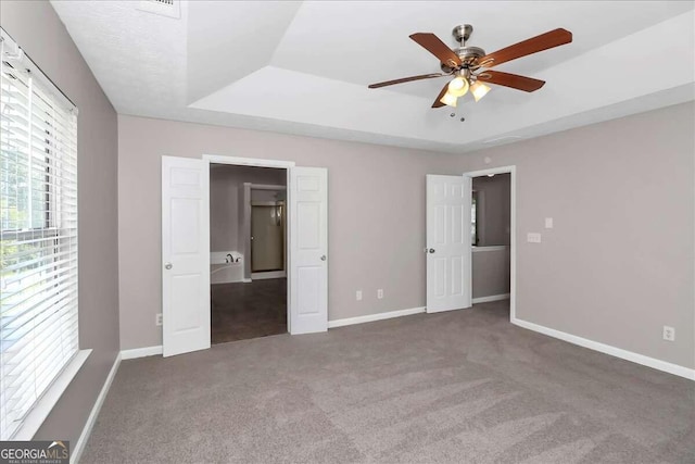 unfurnished bedroom featuring a raised ceiling, ceiling fan, and dark colored carpet