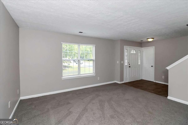 foyer entrance featuring a textured ceiling and dark colored carpet