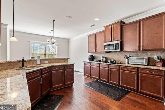 kitchen featuring dark wood-type flooring, an inviting chandelier, hanging light fixtures, light stone countertops, and appliances with stainless steel finishes