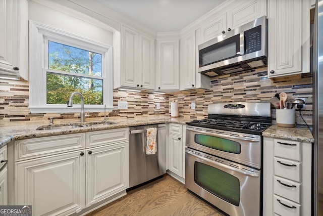 kitchen with white cabinets, appliances with stainless steel finishes, light stone countertops, and sink