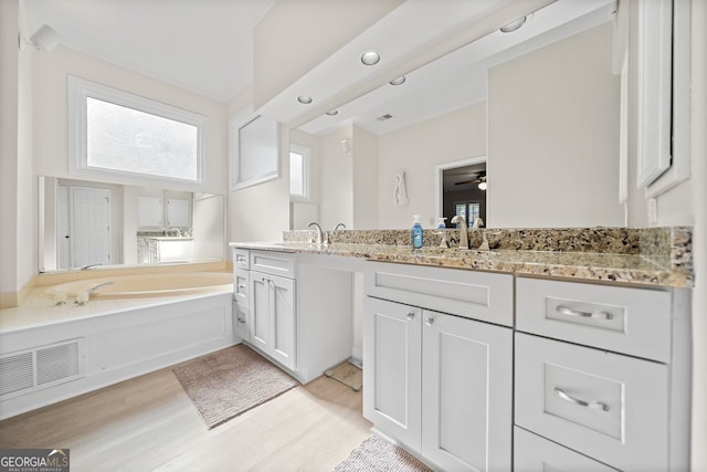 bathroom with a bathing tub, ceiling fan, vanity, and wood-type flooring