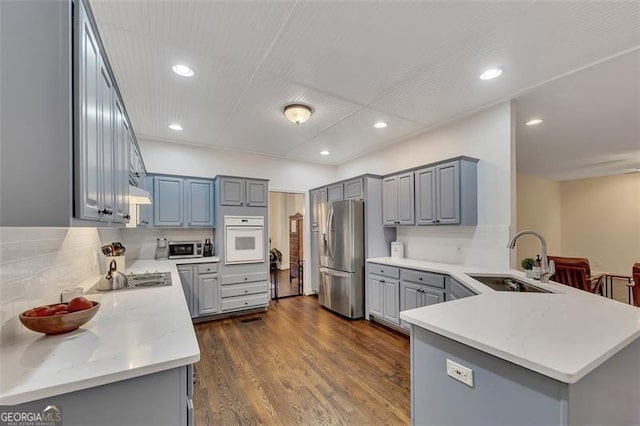 kitchen featuring kitchen peninsula, appliances with stainless steel finishes, gray cabinetry, dark wood-type flooring, and sink