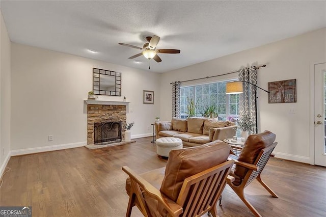 living room featuring a fireplace, wood-type flooring, a textured ceiling, and ceiling fan