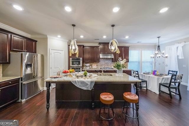 kitchen with a kitchen island with sink, hanging light fixtures, dark wood-type flooring, and appliances with stainless steel finishes