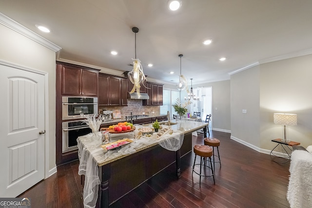 kitchen with decorative light fixtures, a center island with sink, dark wood-type flooring, and light stone counters