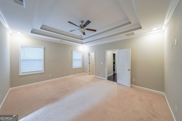 unfurnished bedroom featuring ceiling fan, ornamental molding, light carpet, and a tray ceiling