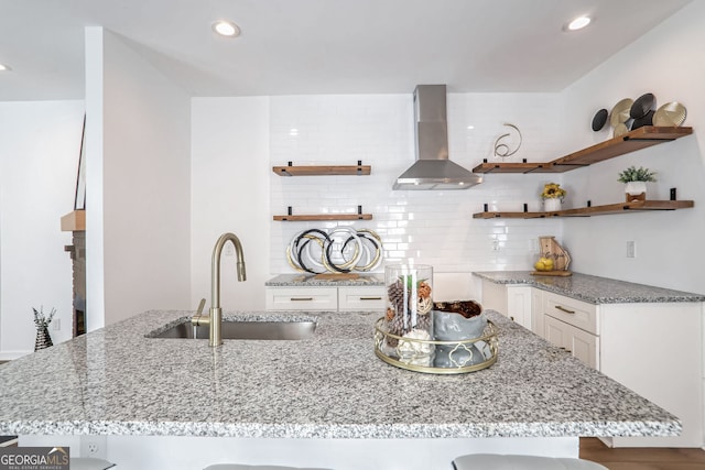 kitchen with a kitchen bar, sink, wall chimney range hood, hardwood / wood-style flooring, and white cabinets