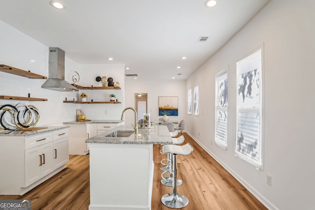 kitchen with sink, light hardwood / wood-style floors, a kitchen island with sink, white cabinets, and exhaust hood