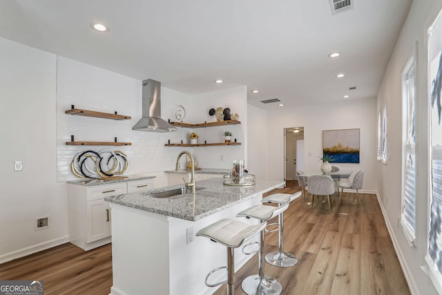 kitchen featuring a wealth of natural light, sink, wall chimney exhaust hood, light hardwood / wood-style flooring, and white cabinets