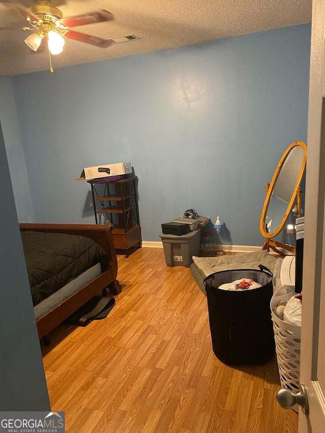 bedroom with a textured ceiling, ceiling fan, and light wood-type flooring