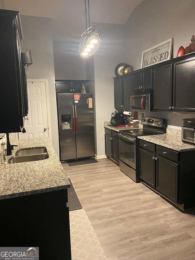 kitchen featuring appliances with stainless steel finishes, pendant lighting, sink, light hardwood / wood-style floors, and light stone countertops