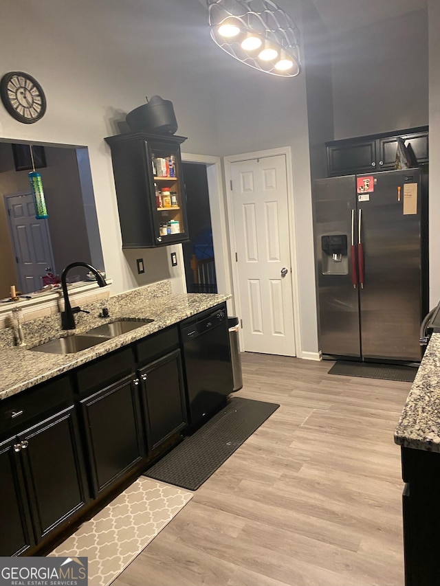 kitchen featuring black dishwasher, sink, light hardwood / wood-style floors, stainless steel refrigerator with ice dispenser, and light stone countertops