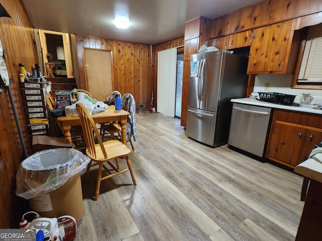 kitchen with wood walls, stainless steel appliances, and light hardwood / wood-style flooring