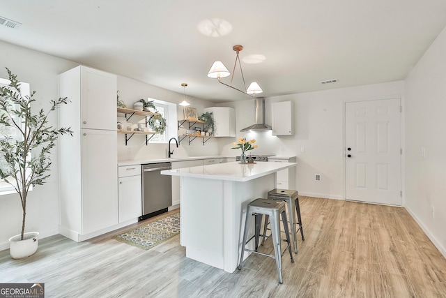 kitchen with dishwasher, white cabinetry, a kitchen island, and wall chimney range hood