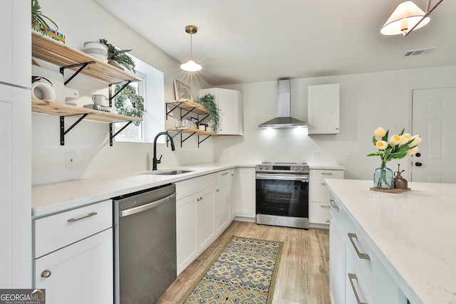 kitchen with appliances with stainless steel finishes, sink, wall chimney range hood, pendant lighting, and white cabinets