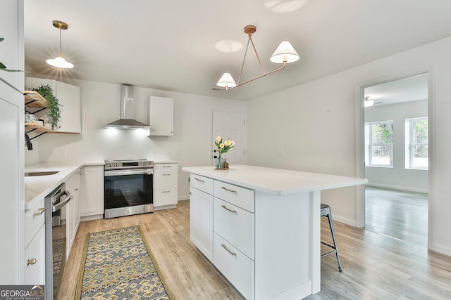 kitchen with light wood-type flooring, wall chimney exhaust hood, stainless steel appliances, pendant lighting, and white cabinets