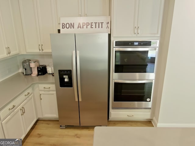 kitchen featuring backsplash, appliances with stainless steel finishes, white cabinetry, and light hardwood / wood-style flooring