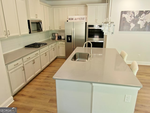 kitchen with a center island with sink, stainless steel appliances, backsplash, white cabinets, and sink