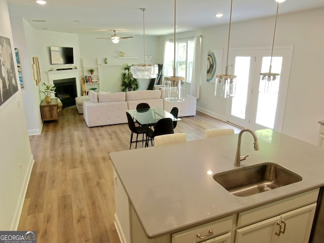 kitchen with an island with sink, sink, hanging light fixtures, ceiling fan, and light hardwood / wood-style flooring