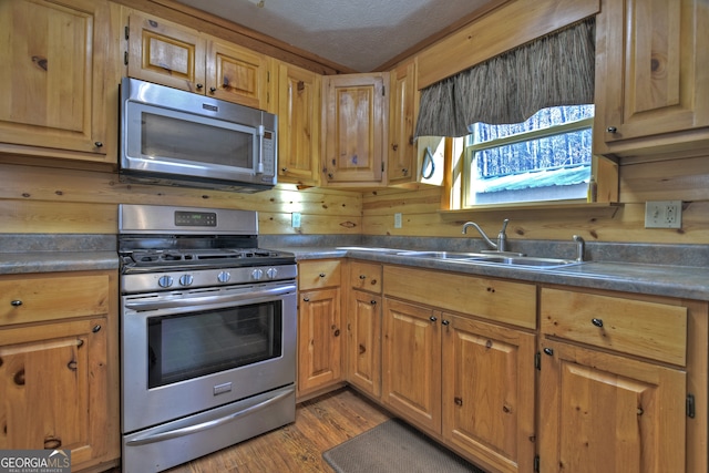 kitchen with sink, wooden walls, light wood-type flooring, a textured ceiling, and appliances with stainless steel finishes