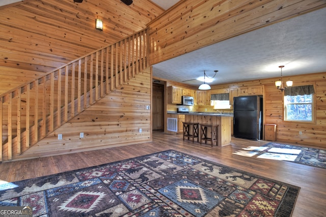 unfurnished living room featuring dark hardwood / wood-style floors, wooden walls, and an inviting chandelier