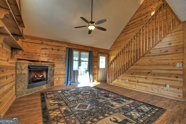 living room with dark hardwood / wood-style flooring, vaulted ceiling, ceiling fan, a fireplace, and wood walls