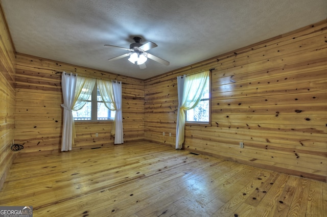 unfurnished room featuring a textured ceiling, light hardwood / wood-style flooring, a wealth of natural light, and wooden walls