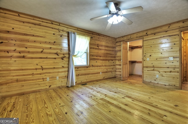 unfurnished bedroom with light hardwood / wood-style floors, a spacious closet, a closet, and wood walls