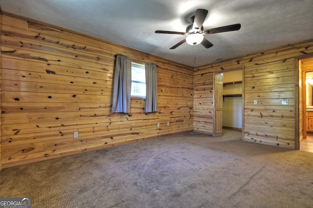 unfurnished bedroom featuring ceiling fan, carpet floors, wooden walls, and a closet