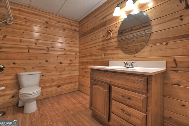 bathroom featuring hardwood / wood-style floors, vanity, a drop ceiling, wooden walls, and toilet