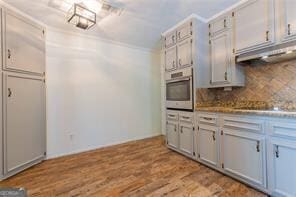 kitchen with black electric cooktop, decorative backsplash, stainless steel oven, and light wood-type flooring