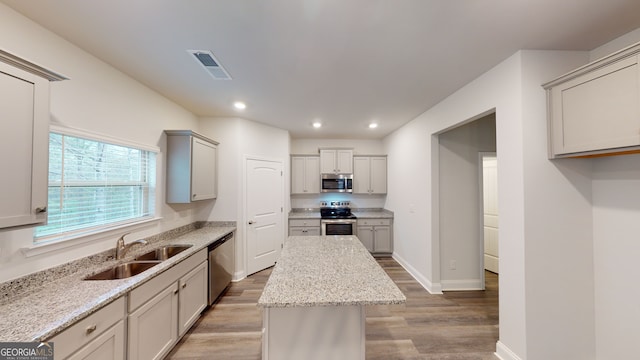 kitchen featuring hardwood / wood-style floors, sink, appliances with stainless steel finishes, a kitchen island, and light stone counters