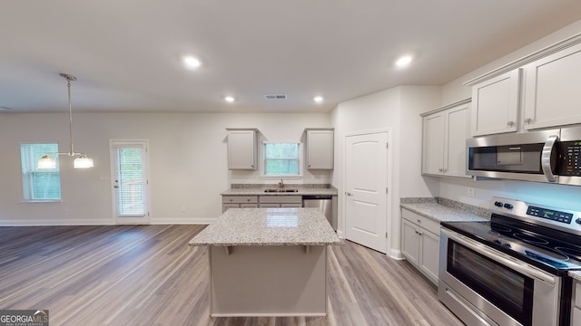 kitchen featuring light stone countertops, light wood-type flooring, stainless steel appliances, sink, and a center island