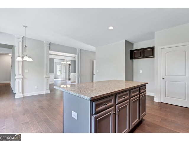 kitchen featuring light stone counters, dark hardwood / wood-style floors, decorative columns, dark brown cabinets, and a kitchen island