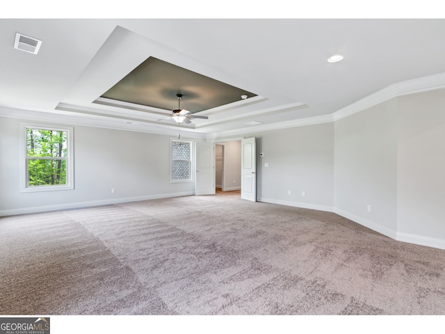 empty room with a raised ceiling, light carpet, ceiling fan, and ornamental molding