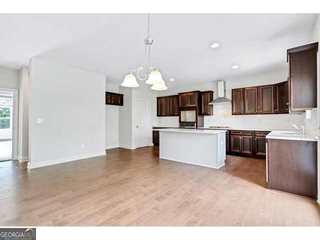 kitchen featuring sink, wall chimney exhaust hood, hanging light fixtures, an inviting chandelier, and a kitchen island