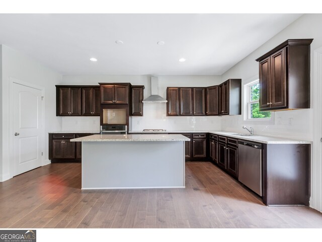 kitchen featuring dark brown cabinetry, sink, a center island, wall chimney range hood, and appliances with stainless steel finishes