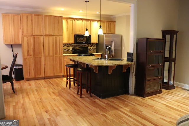 kitchen featuring light stone countertops, light hardwood / wood-style flooring, decorative light fixtures, a kitchen bar, and black appliances