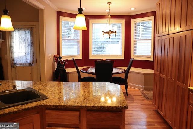 kitchen with light wood-type flooring, crown molding, light stone counters, and pendant lighting