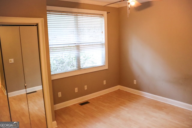 unfurnished bedroom featuring ceiling fan, wood-type flooring, ornamental molding, and a closet