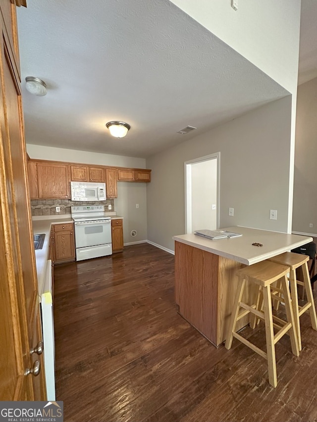 kitchen with dark hardwood / wood-style floors, a kitchen bar, white appliances, and kitchen peninsula