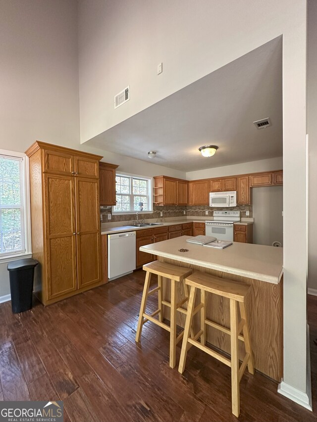 kitchen with dark hardwood / wood-style flooring, backsplash, white appliances, sink, and a breakfast bar area